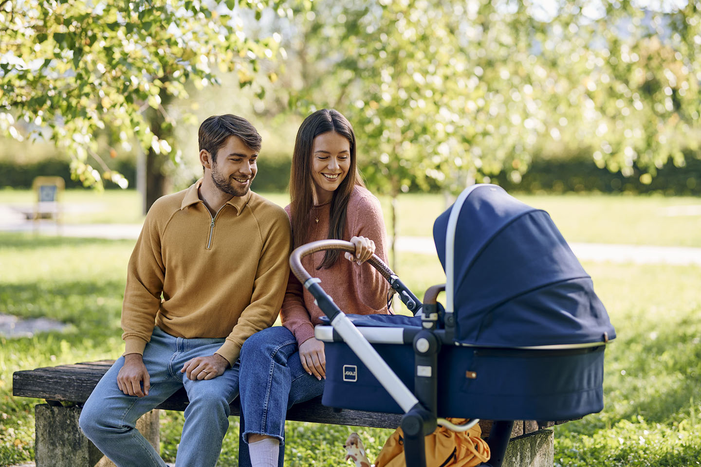 Roditelji s kolicima uživaju u mirnom trenutku na klupi u parku.