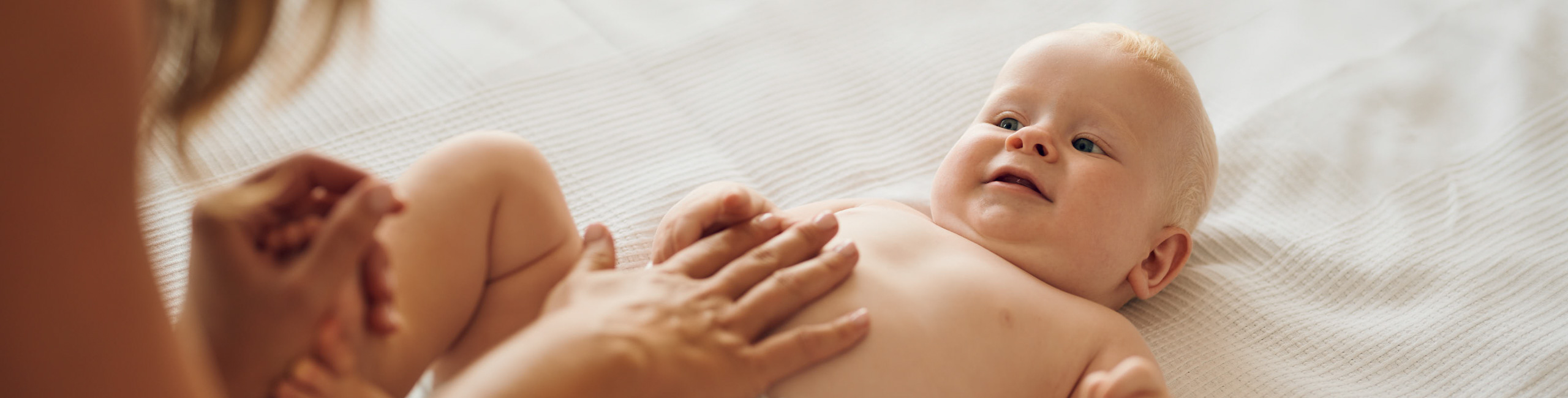 Dojenče leži na postelji, mama mu mijenja pelenu – briga i njega.