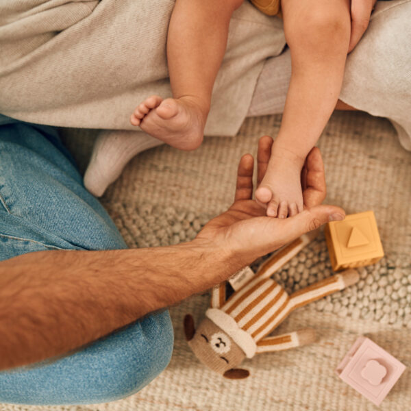 Tata drži bebino stopalo – sretni trenuci igre na mekanom tepihu.