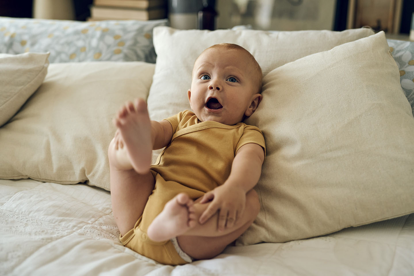 Dojenče leži na postelji i istražuje nogama – razvoj motorike i zabava.